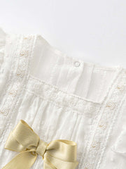 Close-up of baby girls' floral embroidery onesie with intricate lace detailing and a satin gold bow for a luxurious spring look.