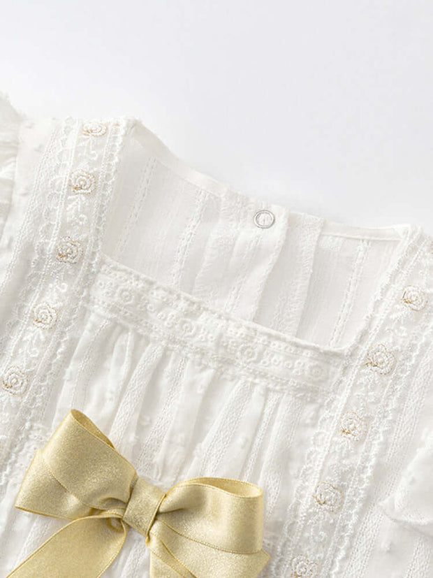 Close-up of baby girls' floral embroidery onesie with intricate lace detailing and a satin gold bow for a luxurious spring look.