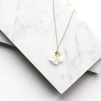 Catalina Necklace - 14k Gold Filled with white petal charms, displayed on a marble background. Sustainable and handmade using recycled metals.