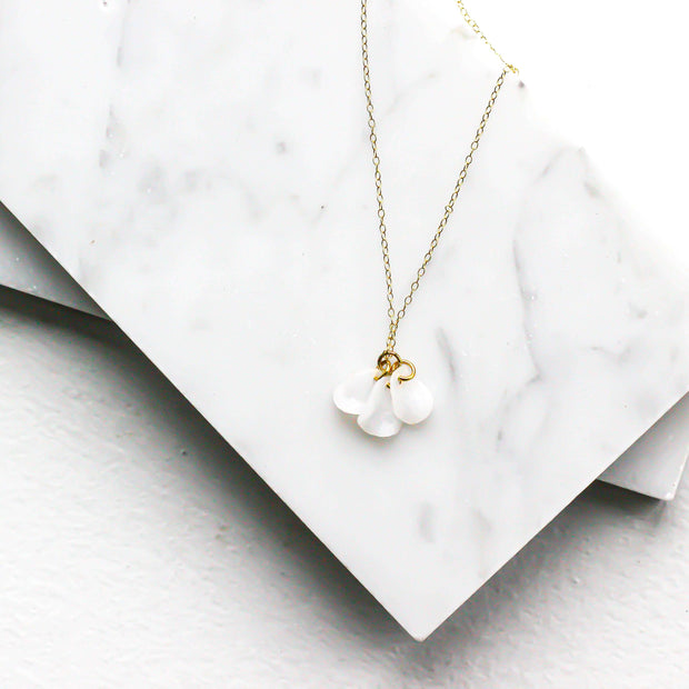 Catalina Necklace - 14k Gold Filled with white petal charms, displayed on a marble background. Sustainable and handmade using recycled metals.