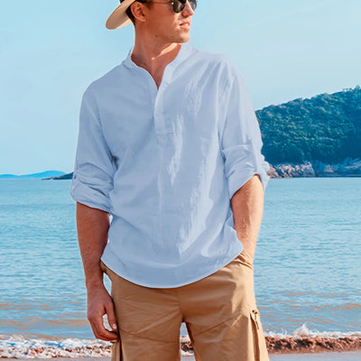 Man wearing a light blue shirt, beige shorts, and a straw hat on a beach.