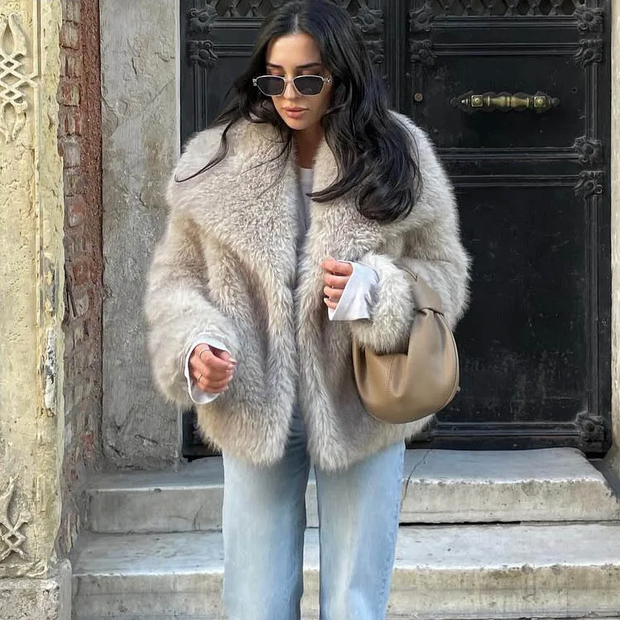Woman wearing a fur coat and sunglasses, standing in front of a black door.