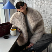 Person wearing a fluffy beige coat sitting at a table with a cup and handbag.