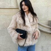 Woman wearing a beige fur coat holding a black clutch against a stone wall.