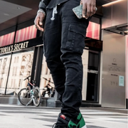 Person wearing black cargo pants walking on a street with a Victoria's Secret store in the background.