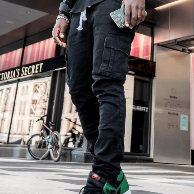 Person wearing black cargo pants walking on a street with a Victoria's Secret store in the background.